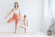 © Вадим Каштанов - Young mother practices yoga with her daughter. Children's yoga. Vrikshasana pose. Couples yoga.