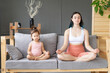© Вадим Каштанов - Mom and little daughter practice yoga in lotus position on sofa. Emotional connection, empathy and understanding, love and unity. Gray interior background.