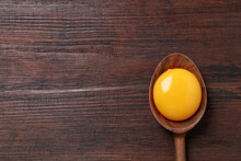 Spoon with raw egg yolk on wooden table, top view. Space for text