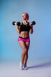 © Antipina - Stylish sports background. Sporty modern woman exercising with dumbbells strong with muscles. Blue fitness neon banner. Workout gym. Girl powerful in sportswear. Bodybuilding. Pink hair