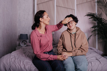 communication brunette mom with teenage daughter sitting on the bed in the room