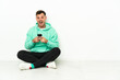 © luismolinero - Young handsome caucasian man sitting on the floor surprised and sending a message