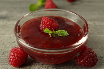 Wall Mural - Glass bowl of raspberry jam with ingredients on gray textured background