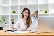 © kamiphotos - Beautiful Asian businesswoman sitting in her private office, chatting with her partner via laptop and checking documents, she is a female executive of a startup company. Financial management concept.