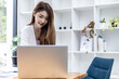 © kamiphotos - A beautiful Asian businesswoman standing in a room, she is talking business with her partner through a laptop messenger, she is a female executive of a startup company. Concept of financial management