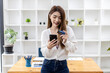 © kamiphotos - Beautiful Asian woman standing with smart phone and credit card, she fills in credit card information to pay for goods and services, online shopping concept pay by credit card and use via smartphone.