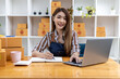 © kamiphotos - A beautiful Asian business owner opens an online store, she is checking orders from customers via laptop, sending goods through a courier company, concept of a woman opening an online business.