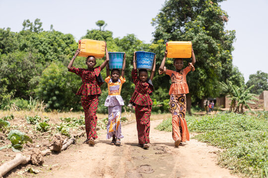 group of four strong beautifully dressed black african girls carrying water containers on their head
