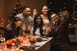 © Syda Productions - holidays, party and celebration concept - multiethnic group of happy friends having christmas dinner at home and taking selfie with smartphone
