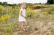 © Sviatlana - A happy little girl in a white dress stands on a field with yellow flowers and smiles on a warm day