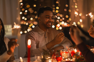 Wall Mural - holidays and celebration concept - multiethnic group of happy friends with sparklers having christmas dinner at home