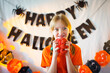 © Анна Молько - girl with pigtails having fun on a background of Halloween attributes. knitted orange pumpkins. preparation for the holiday. garlands on the walls.