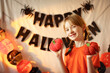 © Анна Молько - girl with pigtails having fun on a background of Halloween attributes. knitted orange pumpkins. preparation for the holiday. garlands on the walls.