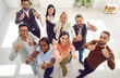 © Studio Romantic - Diverse team of happy motivated young mixed race business people standing in office, looking up, smiling and giving thumbs up all together. High angle, from above, top view. Teamwork, success concept