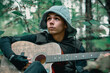 © ISliM - The guy in the hood plays guitar in the woods against the background of trees