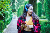 Fototapeta Kwiaty - brunette girl walking through the park gardens listening to music with headphones