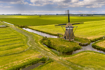 Canvas Print - Old wooden windmill in green agricultural grassland