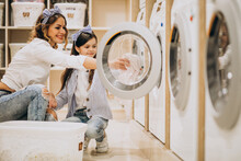 Mother With Daughter Doing Laundry At Self Serviece Laundrette