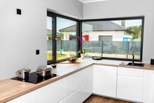 Large Corner Window In A Modern Kitchen With Built-in Cabinets Against The Wall With White Fronts.