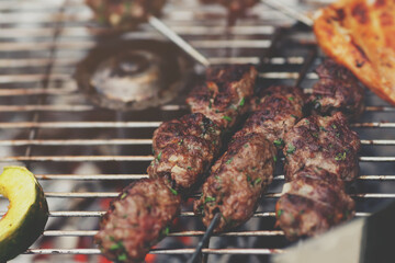 closeup on fresh kofta lamb meat spits with mint that are grilled on a charcoal grill - matte barbecue scenery with selective focus