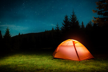 Wall Mural - Orange illuminated tent in dark night forest with night sky and stars