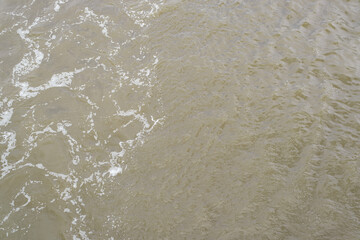 Dirty brown water of a river or sea with foam, sewage splashing, top view