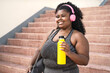 © Alessandro Biascioli - Happy plus size African woman doing workout routine while listening music with wireless headphones outdoor