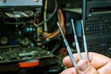 Man's hand holding three precision screwdrivers to repair electronic components.