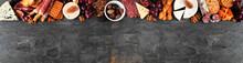 Assorted Cheese And Meat Appetizers. Overhead View Top Border On A Dark Slate Banner Background With Copy Space.