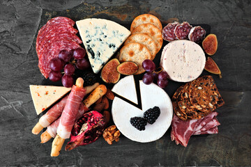 Wall Mural - Charcuterie platter of assorted meats, cheeses and appetizers. Above view on a dark slate background.