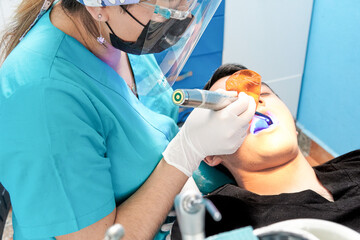 dentist latina woman dressed in blue attending to latina man dressed in black, with ultraviolet light lamp drying a resin or amalgam in patient's mouth, dental office