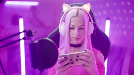 Wall Mural - Portrait of cute Gamer Girl with microphone streaming playing on smartphone 4K