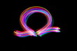 Long exposure photograph of an omega symbol in neon colour in an abstract swirl, parallel lines pattern against a black background. Light painting photography.