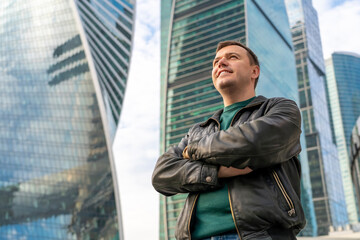 Happy millennial caucasian businessman confident with crossed arms portrait on urban cityscape. Portrait of smiling man standing outside office building with city skyline in background