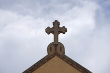 A Decorative Stone Cross On The Rooftop Of A Church With Cloudy Sky Behind