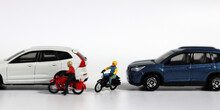 Miniature people and miniature car. A motorcycle rider who forcefully intervenes between two cars. Concept on the importance of safe driving and the risk of accidents.
