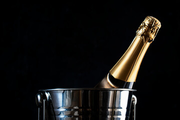 Champagne bottle in silver bucket on black background. Happy New Year or Merry Christmas composition with golden sparkles and bokeh lights