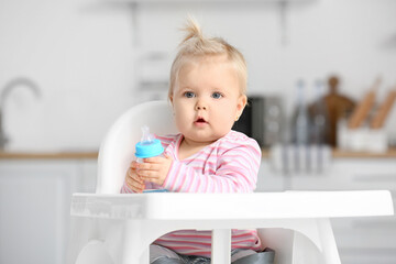 Sticker - Cute baby girl with bottle of water sitting on high chair in kitchen