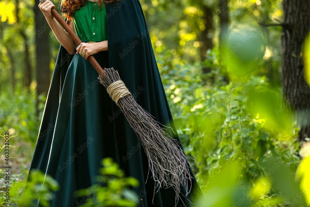 Young witch with broom in green forest