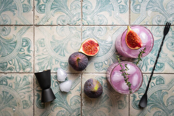 Wall Mural - Purple fig cocktail with ice and thyme on tile background, top view