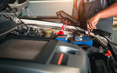 Automobile mechanic repairman hands checking car battery with modern tools digital multimeter in car service center.