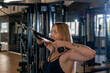© somemeans - Sporty woman in hoody exercising triceps muscles in the gym with pull-down ropes fitness equipment machine attachments.