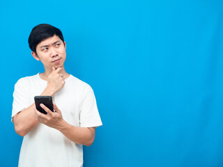 Young man white shirt holding mobile phone gesture thinking and looking at copy space blue background