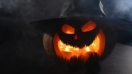 Wall Mural - A creepy pumpkin with a carved grimace in the smoke. Jack o lantern is spinning in the dark.