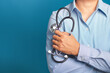 © meeboonstudio - A doctor in a blue shirt holding a stethoscope while standing on a blue background in the studio. Space for text. Medical and healthcare concept