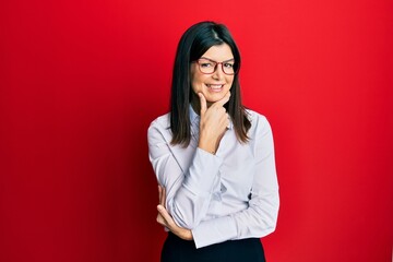 Poster - Young hispanic woman wearing business shirt and glasses looking confident at the camera smiling with crossed arms and hand raised on chin. thinking positive.