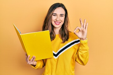 Poster - Young hispanic girl reading a book doing ok sign with fingers, smiling friendly gesturing excellent symbol