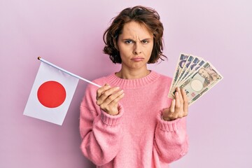 Poster - Young brunette woman holding japan flag and yen banknotes depressed and worry for distress, crying angry and afraid. sad expression.