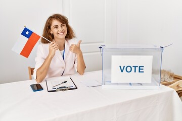 Canvas Print - Beautiful caucasian woman at political campaign election holding chile flag smiling happy and positive, thumb up doing excellent and approval sign