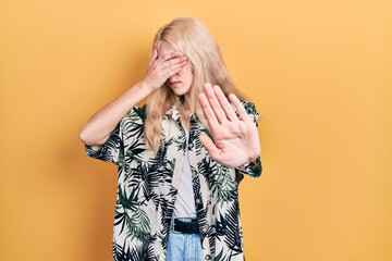 Wall Mural - Beautiful caucasian woman with blond hair wearing tropical shirt covering eyes with hands and doing stop gesture with sad and fear expression. embarrassed and negative concept.